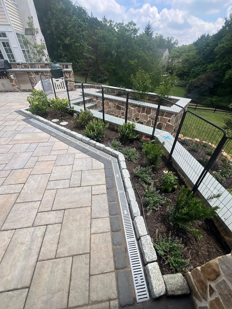 Black welded-wire fence panels with a matching gate set on top of a stone retaining wall around a paver patio in Wayne, PA