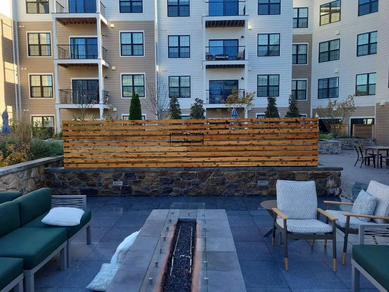Horizontal cedar slat privacy screen mounted on a stone wall in an apartment community courtyard with a fire pit and seating in Edgmont Township, PA