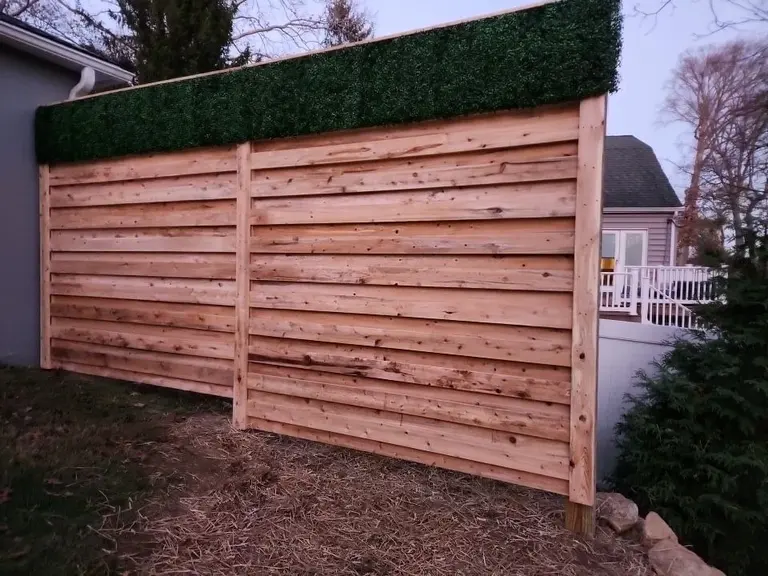 Horizontal cedar privacy fence with an artificial boxwood hedge panel along the top, installed beside a home in West Chester, PA