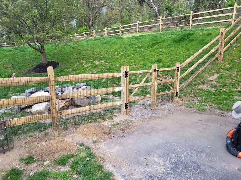 Two-rail split rail fence with welded-wire mesh and a matching gate installed across a sloped lawn in Chester Springs, PA