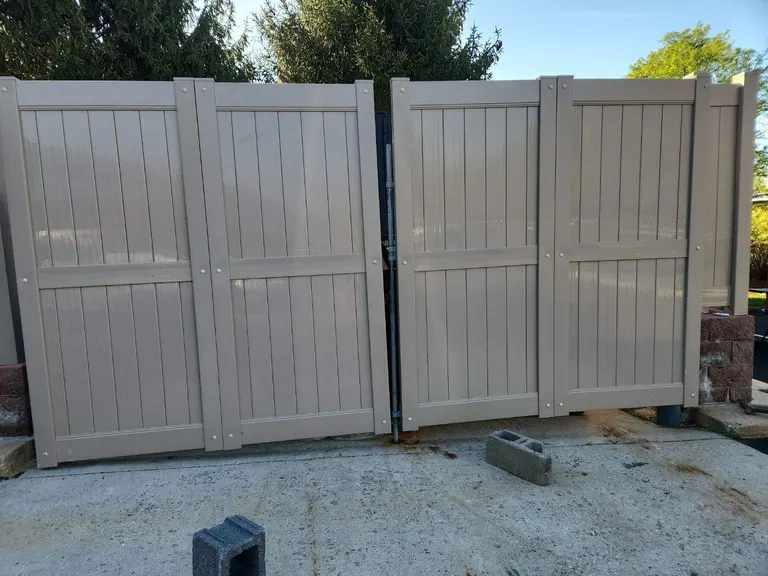 Tan vinyl privacy double gate on a concrete pad between block pillars, installed as an enclosure gate in Newtown Square, PA